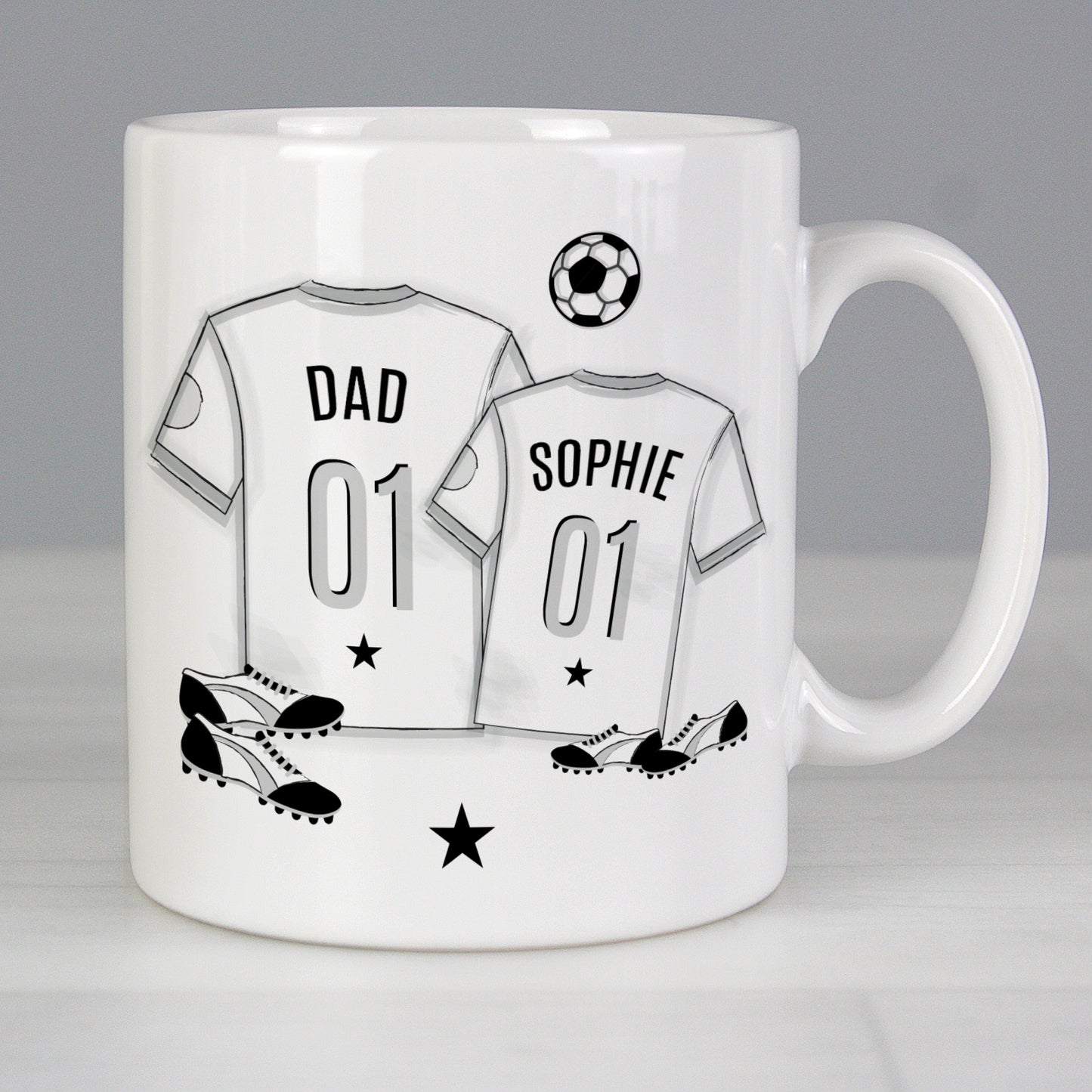 Mug with T-shirt print with personalised name. 1 large T-shirt and 1 small T-shirt with football and football boots in background. 