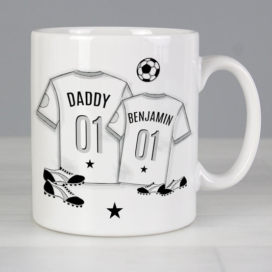 Mug with T-shirt print with personalised name. 1 large T-shirt and 1 small T-shirt with football and football boots in background. 