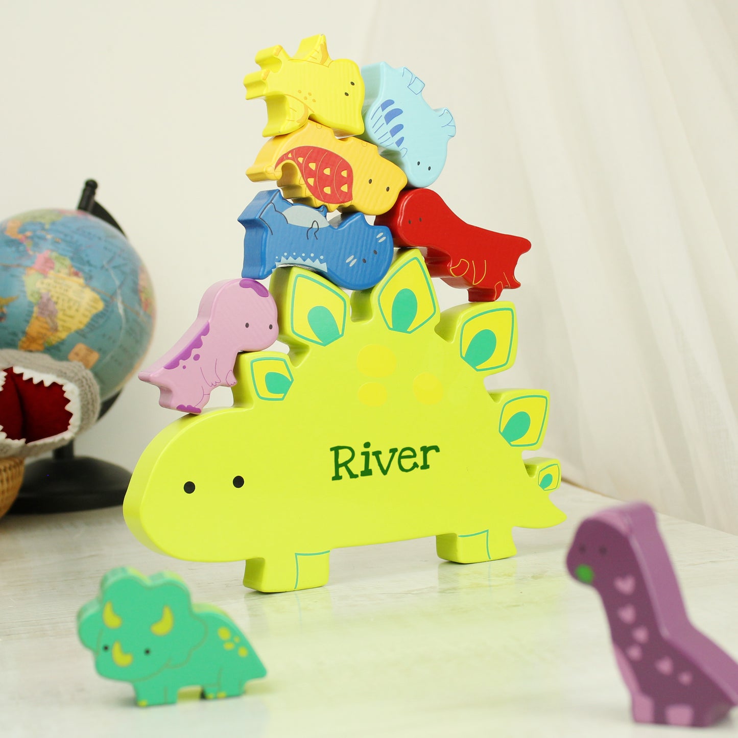 Yellow wooden dinosaur shape personalised with a name and miniature wooden dinosaur shapes in various colours for stacking