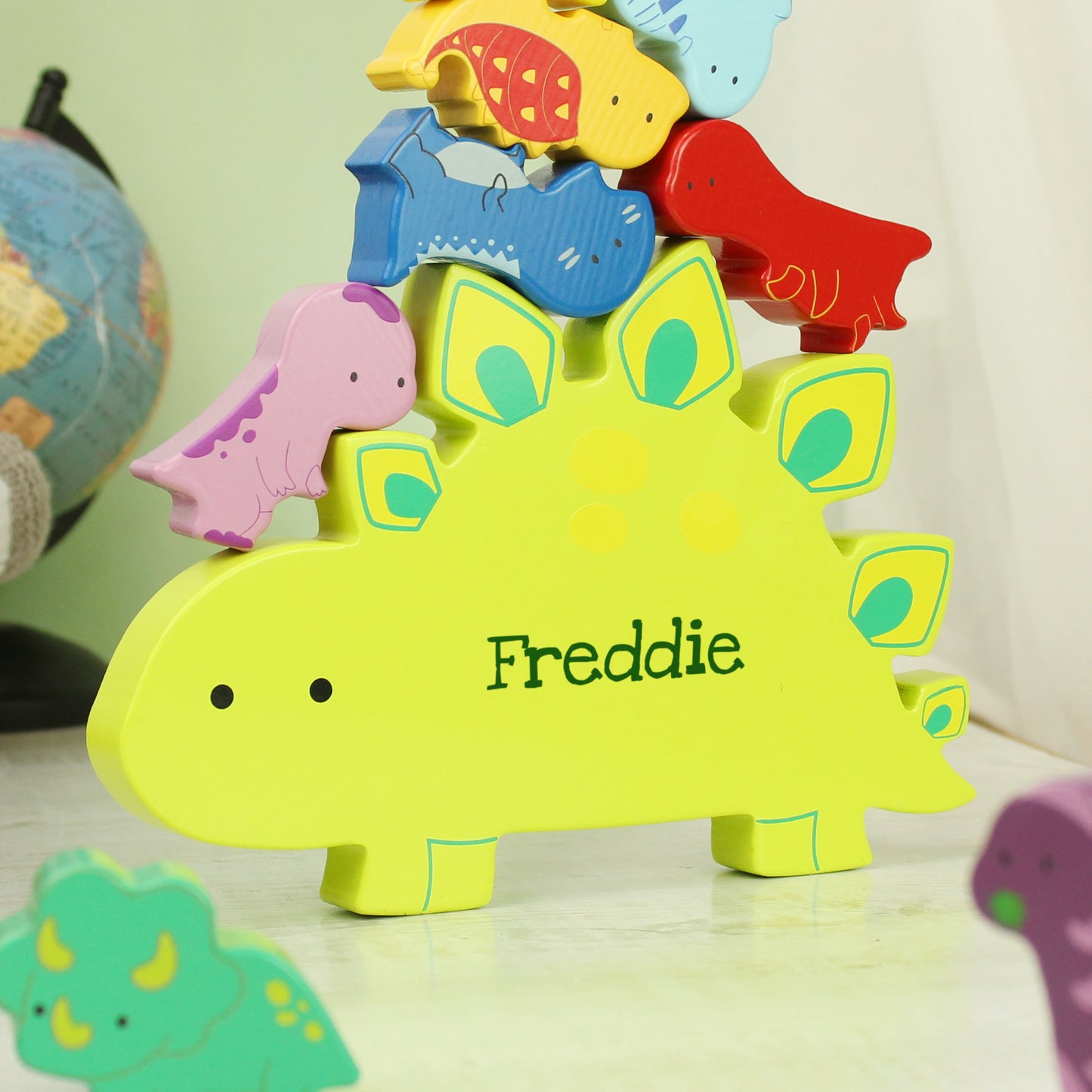 Yellow wooden dinosaur shape personalised with a name and miniature wooden dinosaur shapes in various colours for stacking