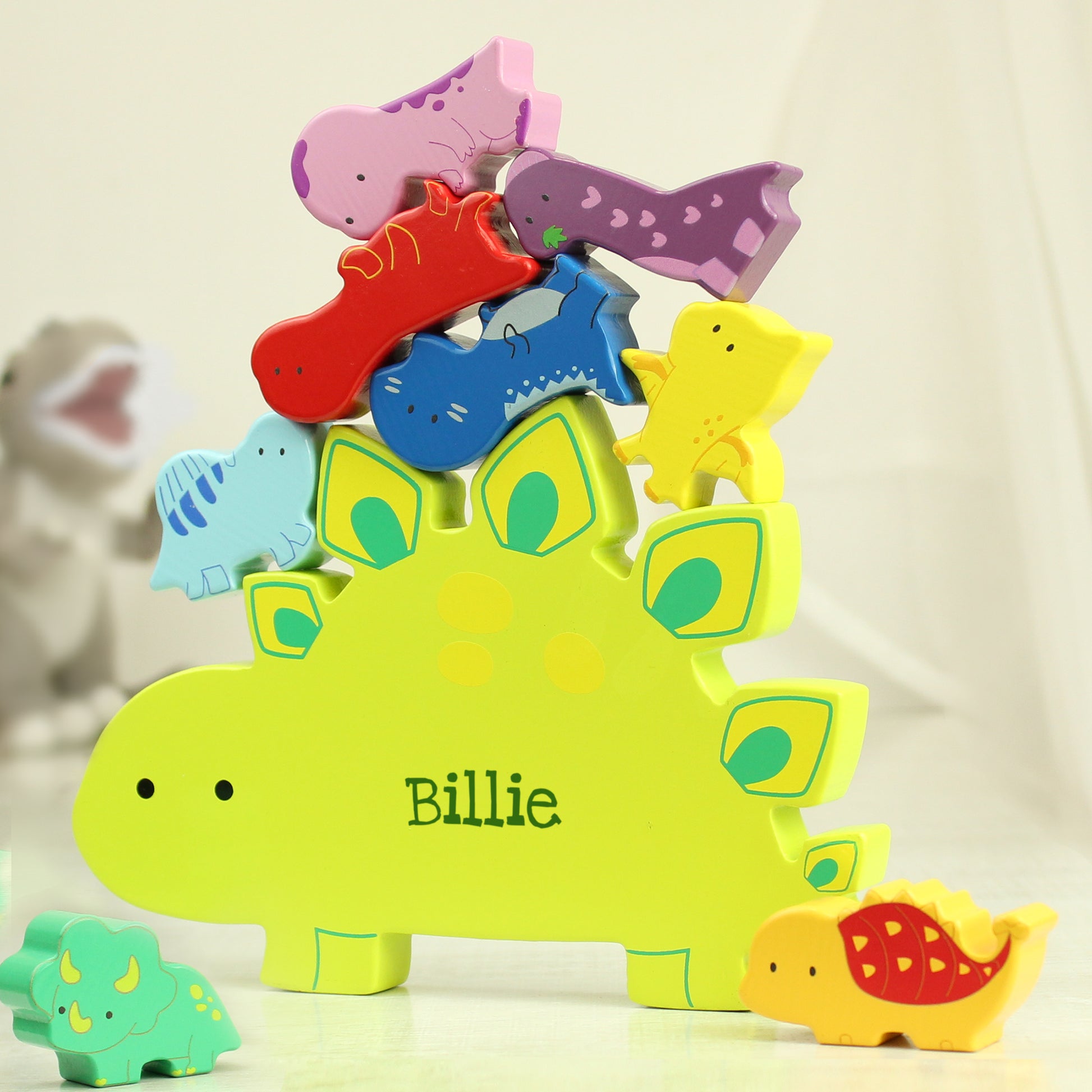 Yellow wooden dinosaur shape personalised with a name and miniature wooden dinosaur shapes in various colours for stacking