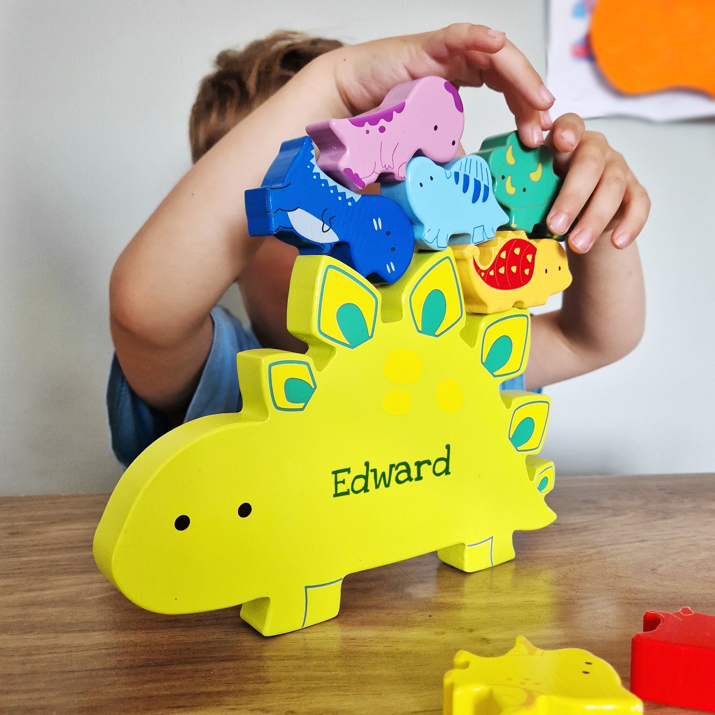 Yellow wooden dinosaur shape personalised with a name and miniature wooden dinosaur shapes in various colours for stacking