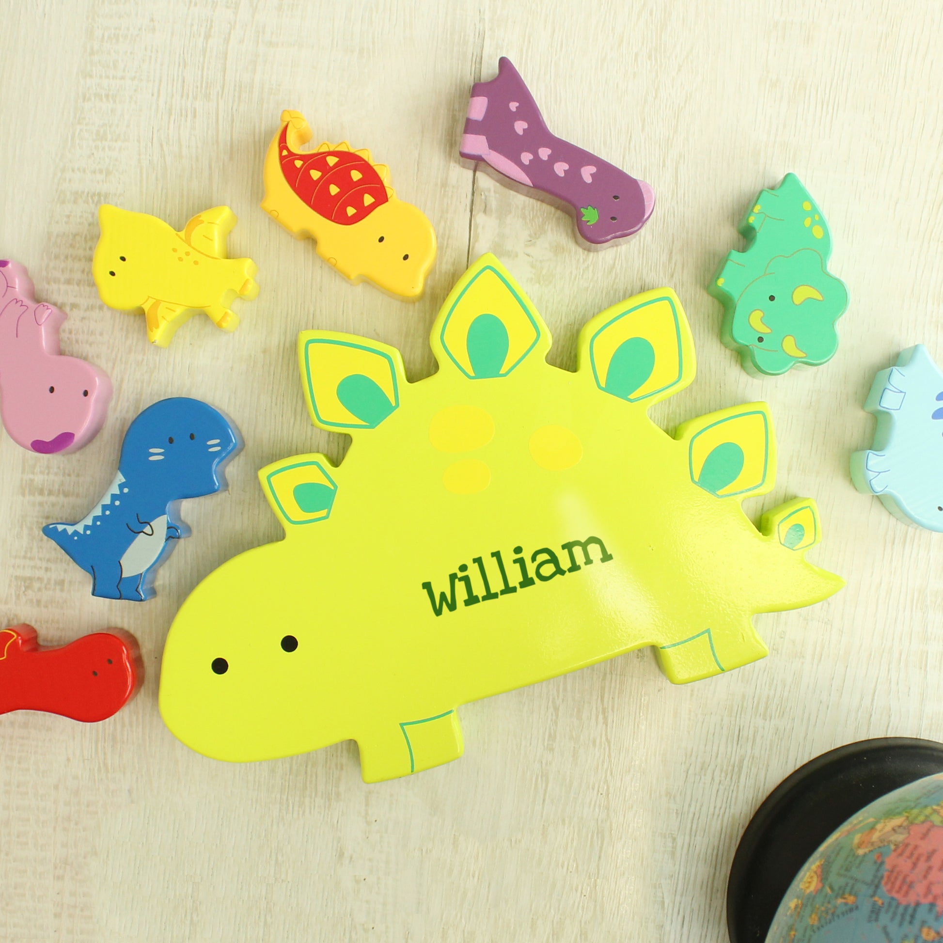 Yellow wooden dinosaur shape personalised with a name and miniature wooden dinosaur shapes in various colours for stacking