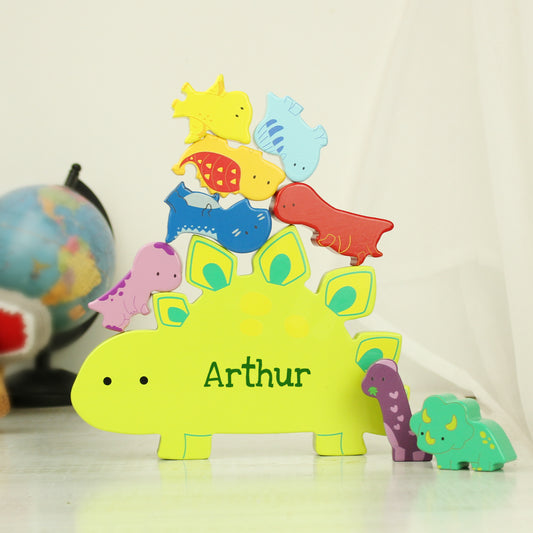 Yellow wooden dinosaur shape personalised with a name and miniature wooden dinosaur shapes in various colours for stacking