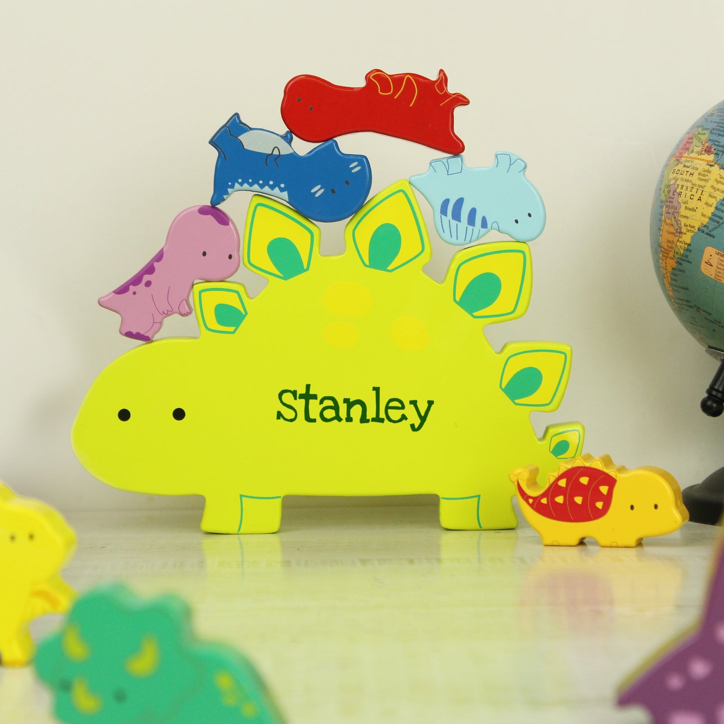 Yellow wooden dinosaur shape personalised with a name and miniature wooden dinosaur shapes in various colours for stacking